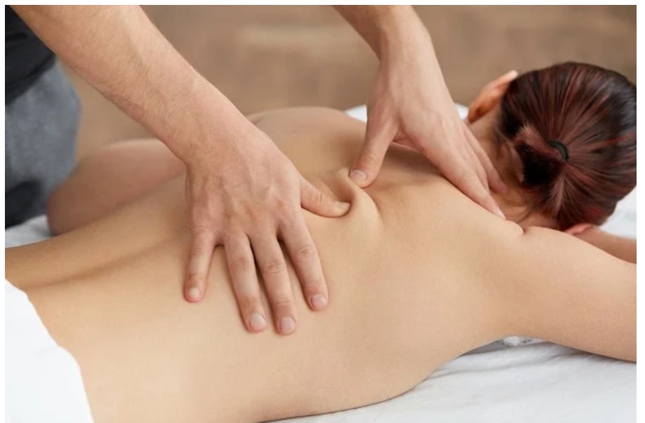 Người đang được xoa bóp trên lưng bởi một đôi tay trên giường massage, không gian thư giãn.