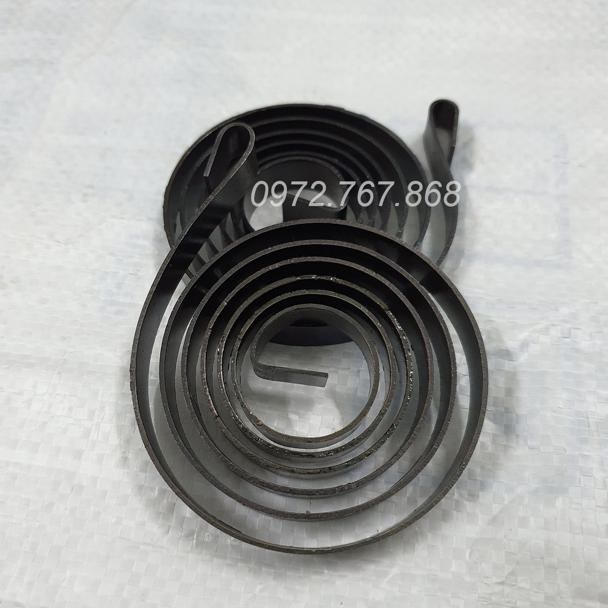 Lò xo máy khoan bàn (bản rộng ~10mm, lá thép dày 1.15mm, đường kính ~72mm)