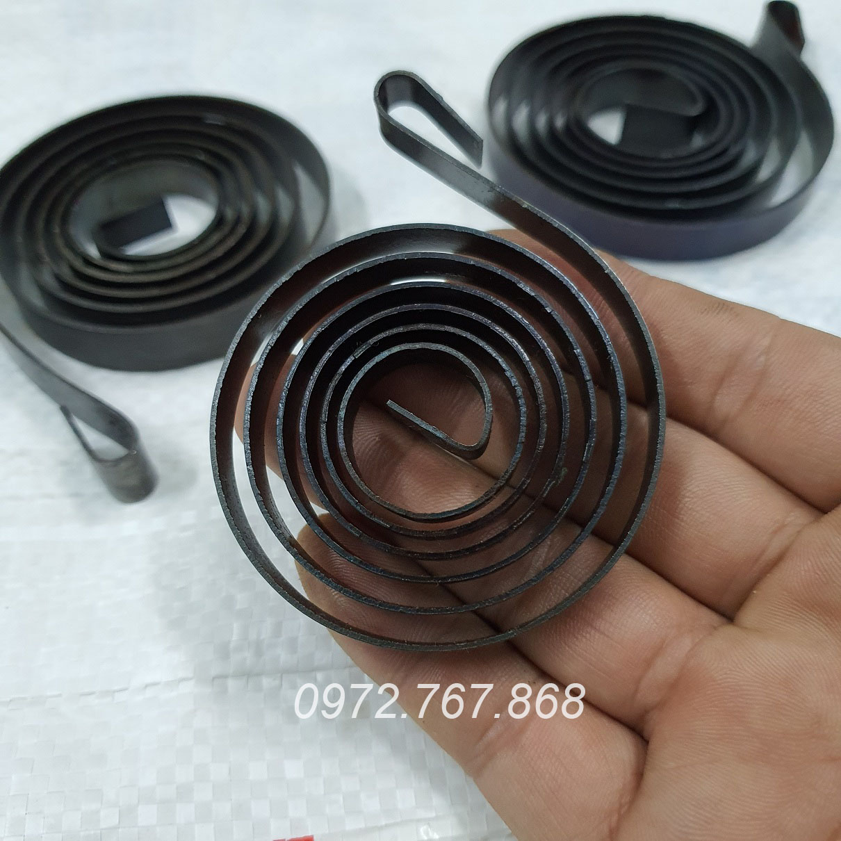 Lò xo máy khoan bàn (bản rộng ~8mm, lá thép dày 0.85mm, đường kính ~59mm)